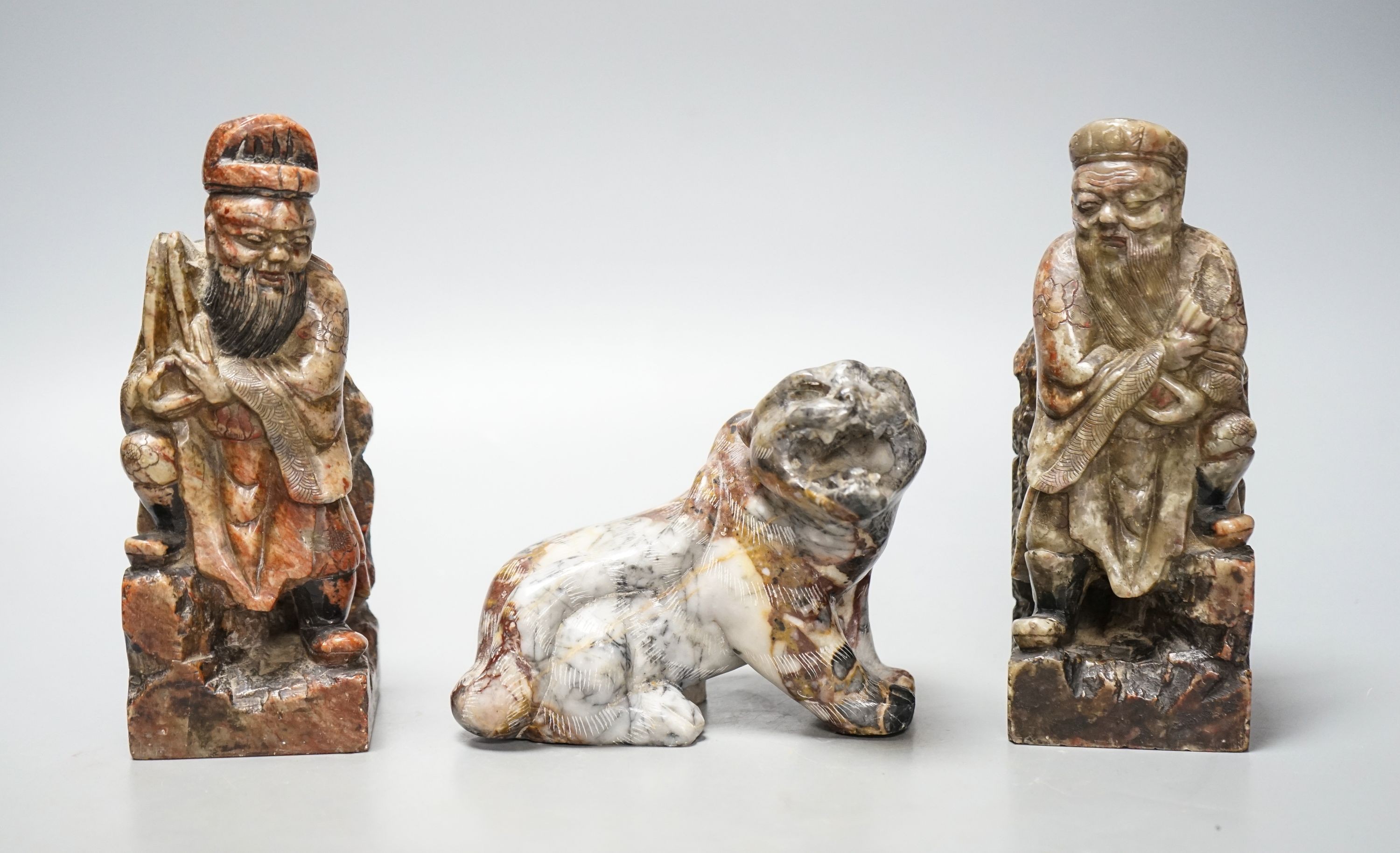A pair of Chinese soapstone figures of immortals, modelled seated on rocky bases and a similar figure of tiger, 12cm